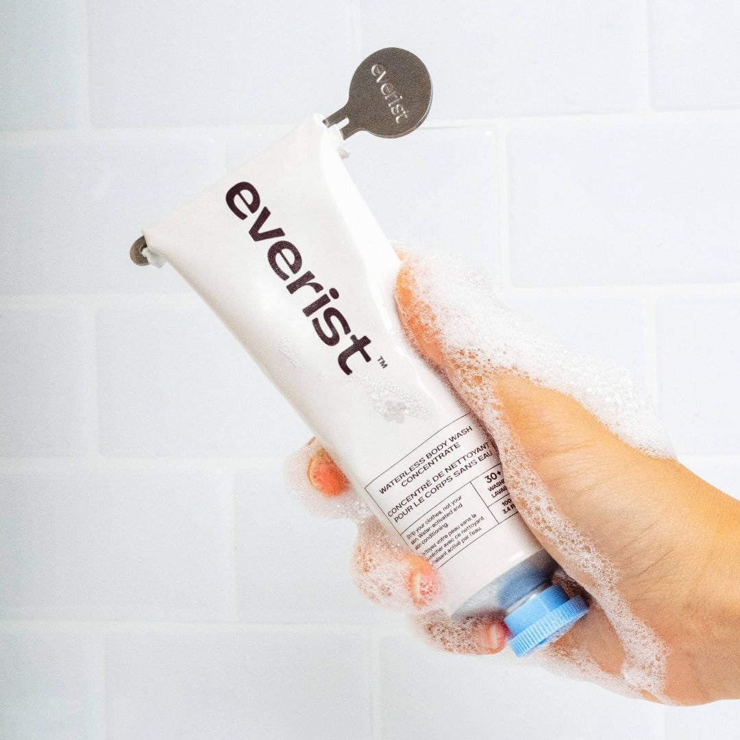 The Body Wash Concentrate, a hand holding the waterless body wash concentrate in a shower with sudsy bubbles.