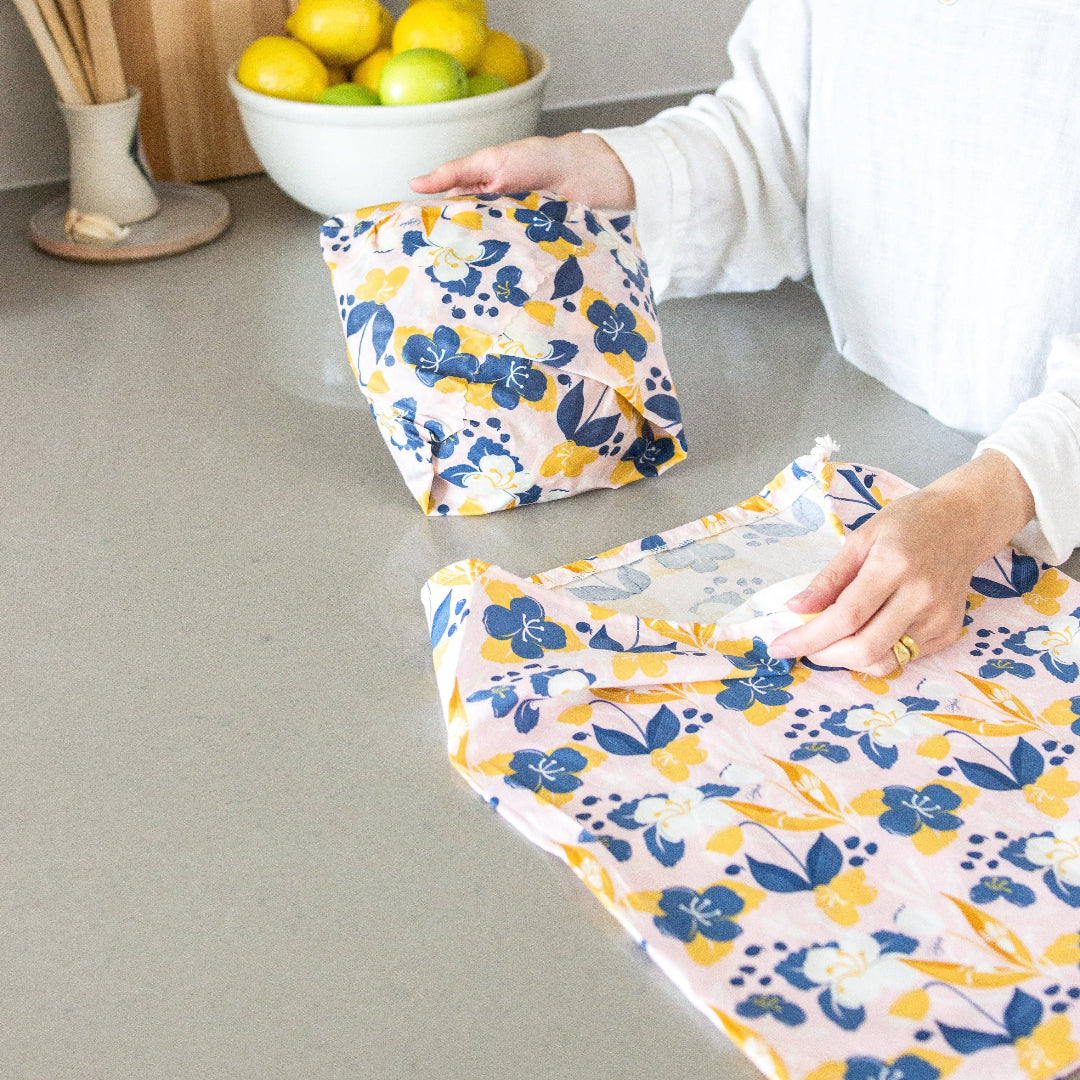 Person using floral-patterned food wraps on a kitchen counter with lemons in the background.