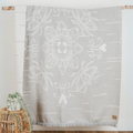 The Birch Bark Reversible Blanket by Mini Tipi, featuring a delicate white birch bark-inspired pattern on a grey background, hanging from a wooden rod. This reversible blanket is available in Ottawa, Ontario, Canada.