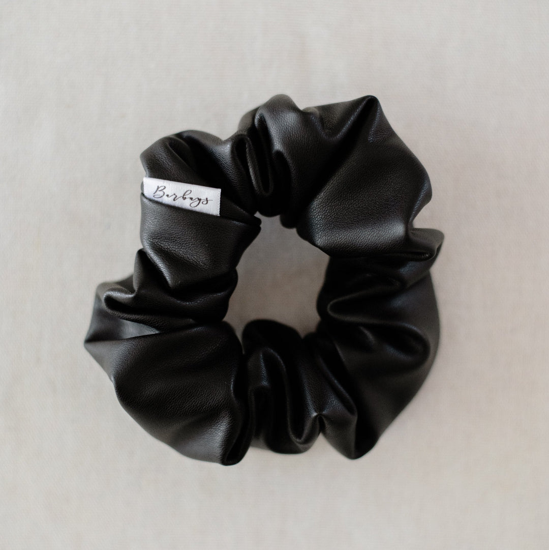Black scrunchie with a brand label on a light gray background