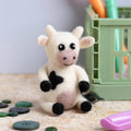 Small cow plush toy on a textured surface with colorful objects in the background