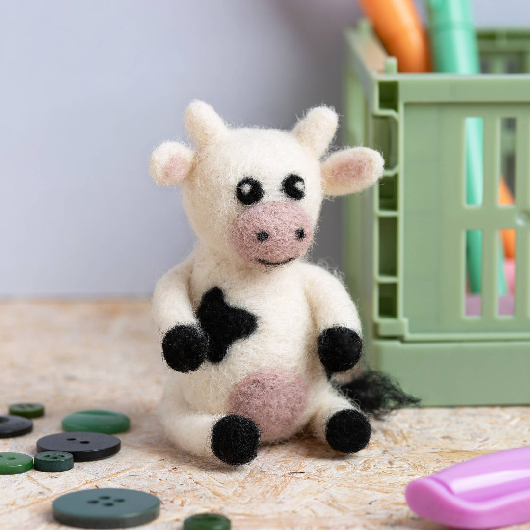 Small cow plush toy on a textured surface with colorful objects in the background