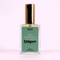 A small glass bottle of perfume with a gold cap. The bottle is transparent and filled with a light-colored liquid. The label on the bottle reads "Draper" in large, black letters. Below the brand name, it lists the fragrance notes: "Teak, Cardamom, Sandalwood."