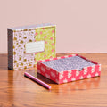 Two patterned boxes with a pink pen on a wooden surface