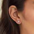 Heart-shaped diamond earring worn by a person with dark hair.