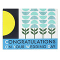 A wedding card with a modern geometric design. The top portion is white with rows of light blue abstract floral or fan shapes, and a large yellow circle against a black background on the left. The bottom section is a solid blue band with white text that reads "CONGRATULATIONS ON YOUR WEDDING DAY".