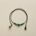 Necklace with black cord and green beads on a beige background