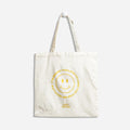A white tote bag with a yellow smiley face design. The text around the smiley face reads: "It's never too late to have the time of your life." The bottom right corner displays the "Epic Blend" logo.