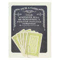A dark grey card with white decorative borders. The top text reads "PICK A CARD" and below it, "YOUR KINDNESS WILL BE REWARDED, A POSITIVE OUTLOOK FORESEEN". At the bottom, five light green and white playing card-like fortunes are fanned out and held by a paperclip.