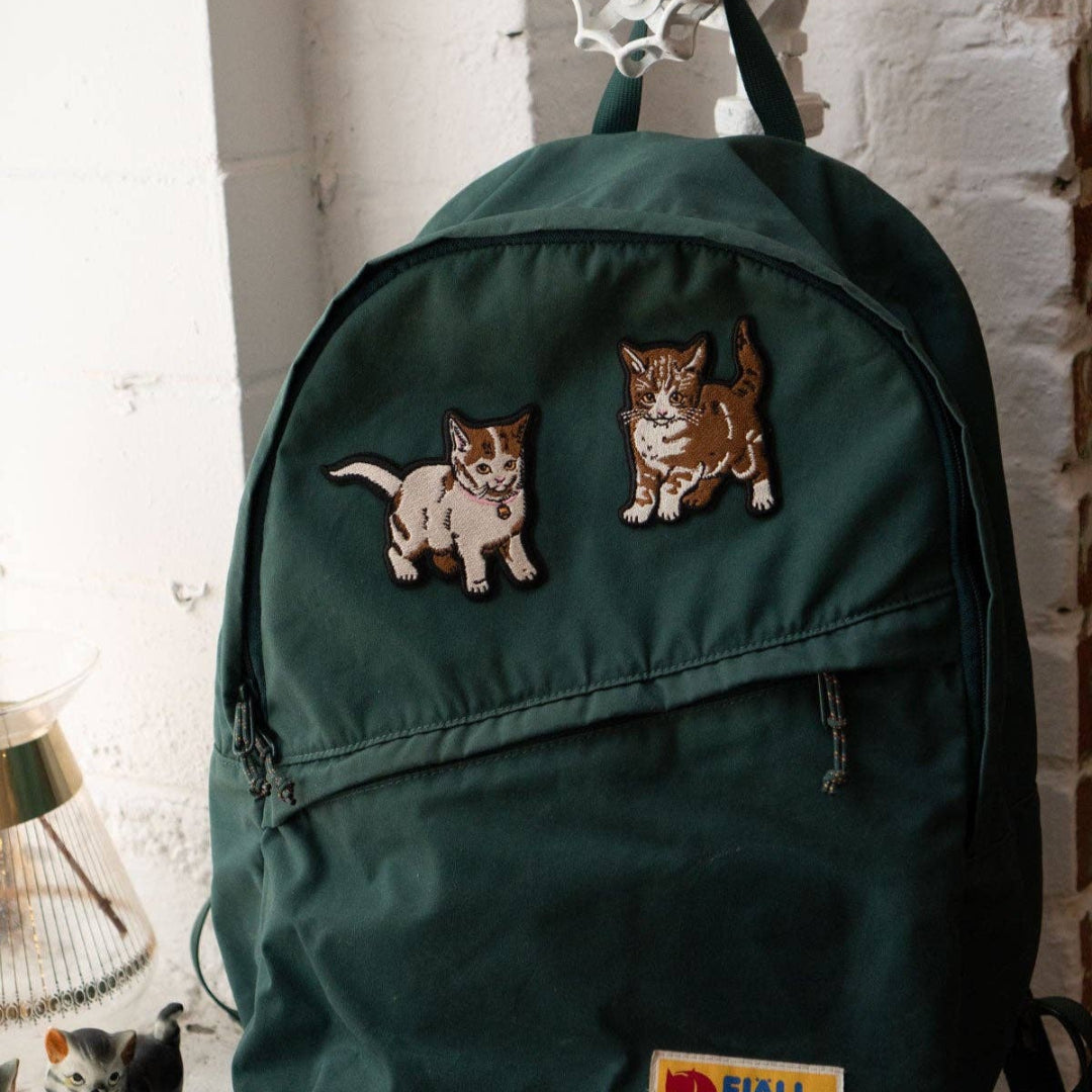 Green backpack with cat-themed patches on a white surface.