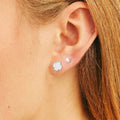 Close-up of an ear wearing a silver flower earring and a pearl earring.