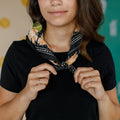 A black bandana with a floral pattern. The pattern features orange flowers and green leaves on a black background.