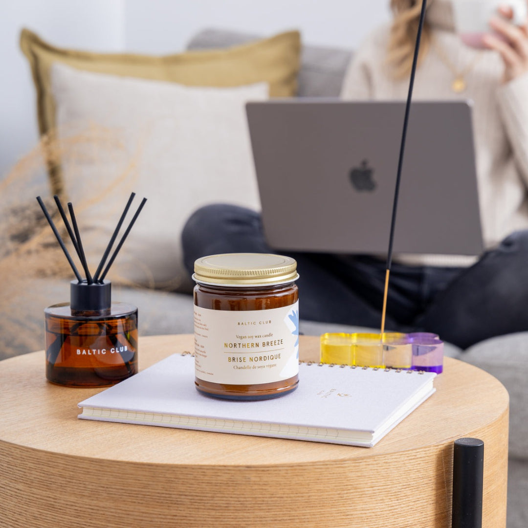 Person using a laptop on a couch with a candle, diffuser, and incense on a table in the foreground.