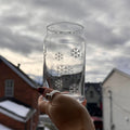 Hand holding a clear glass jar with snowflake designs against a cloudy sky and houses in the background.