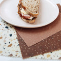 Half-eaten sandwich on a white plate with a brown napkin underneath