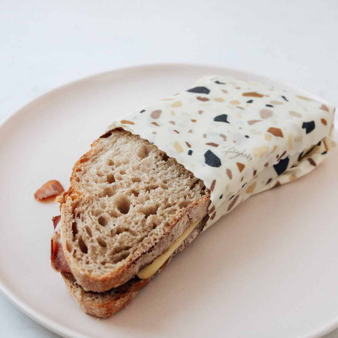 Half-eaten sandwich wrapped in a patterned paper on a white plate