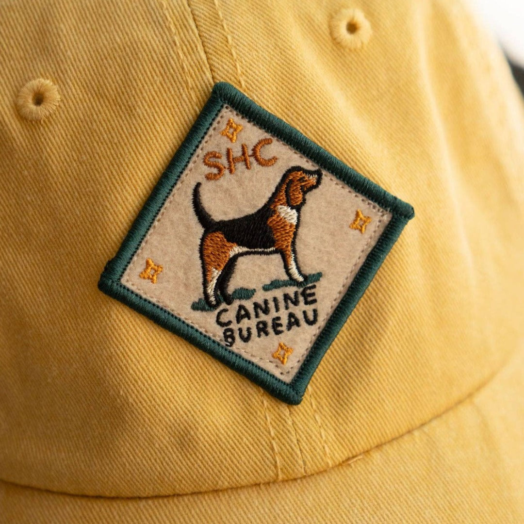 A diamond-shaped embroidered patch with a green border. It features a brown and black beagle standing facing left, with the text "SHC" above and "CANINE BUREAU" below the dog. The patch has four small stars at the corners.