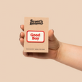 Hand holding a Scout's Honour 'Good Boy' patch against a beige background