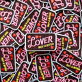 Collection of 'Lover Not a Biter' patches with pink and yellow text on a black background.