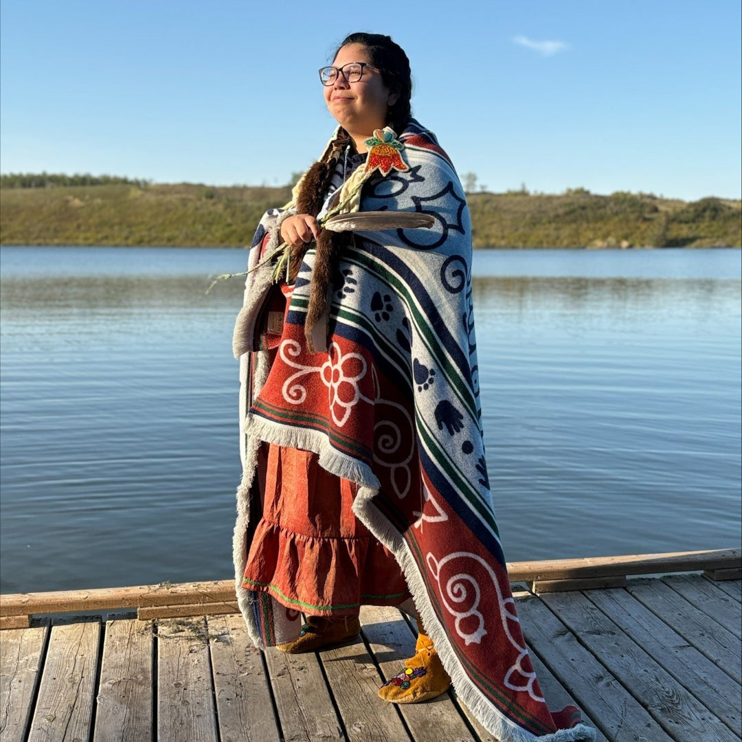 Person standing on a dock by a lake, wearing a colorful patterned blanket.